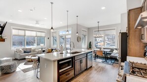 A modern kitchen with a central island, wooden cabinets, and pendant lighting.