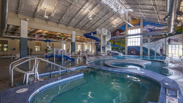 An indoor swimming pool with multiple lanes, a water slide, and a mural on the walls.