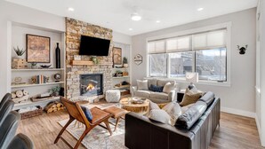 A modern living room with a stone fireplace, comfortable seating, and a large window providing a view of the outdoors.