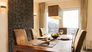 A dining area with a wooden table, six chairs, a fruit bowl, and two wine glasses. - Panorama Lounge (Willingen)