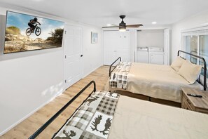 Una habitación con dos camas, ventilador de techo, televisor montado y ventana.