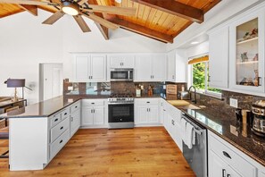 Una cocina amplia con armarios blancos, encimera de granito y techo de madera.