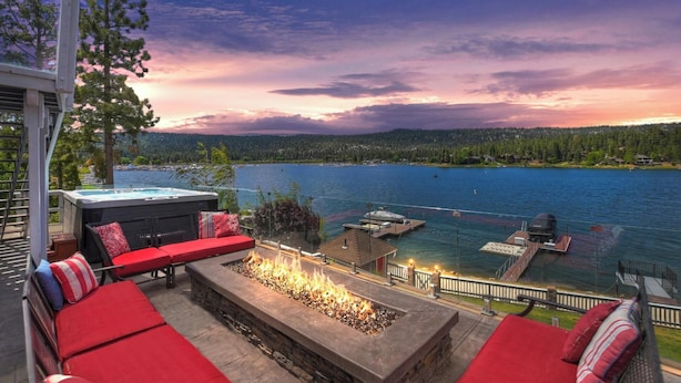 Un patio frente al lago con asientos exteriores, una fogata y un jacuzzi.