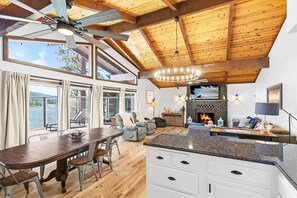 A spacious living area with a fireplace, wooden ceiling beams, a dining table, and a view of the outdoors.