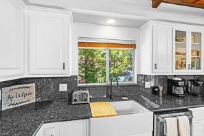 A kitchen with white cabinets, a granite countertop, a window with a view of trees, a toaster, a coffee maker, and a sink.