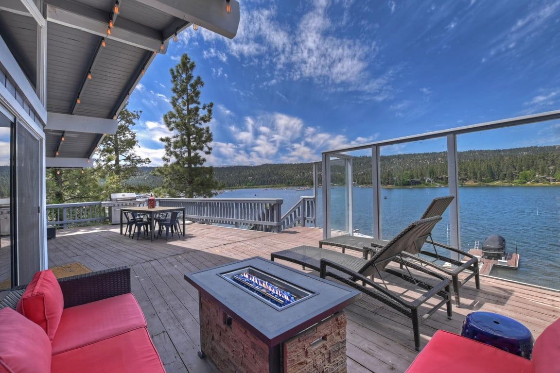 Eine Terrasse mit Gartenmöbeln, einer Feuerstelle und Blick auf einen See und Wald.
