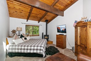 Een slaapkamer met een bed, een televisie, een houten kast en een raam met jaloezieën.