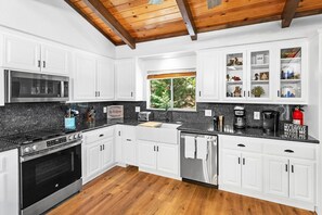 Una cocina moderna con armarios blancos, encimera negra, electrodomésticos de acero inoxidable y techo de madera.
