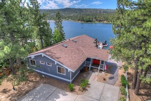 A single-story house with a red roof, a front porch, and a dock extending into a lake.