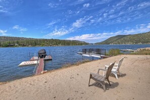 Een terras aan het meer met een barbecue, stoelen en een steiger die het water in loopt.