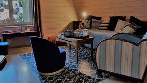 A cozy room with a bed, a desk, a chair, and a window with potted plants.