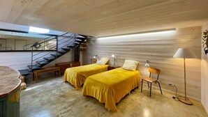 A bedroom with two beds, a wooden ceiling, a staircase, and a lamp.