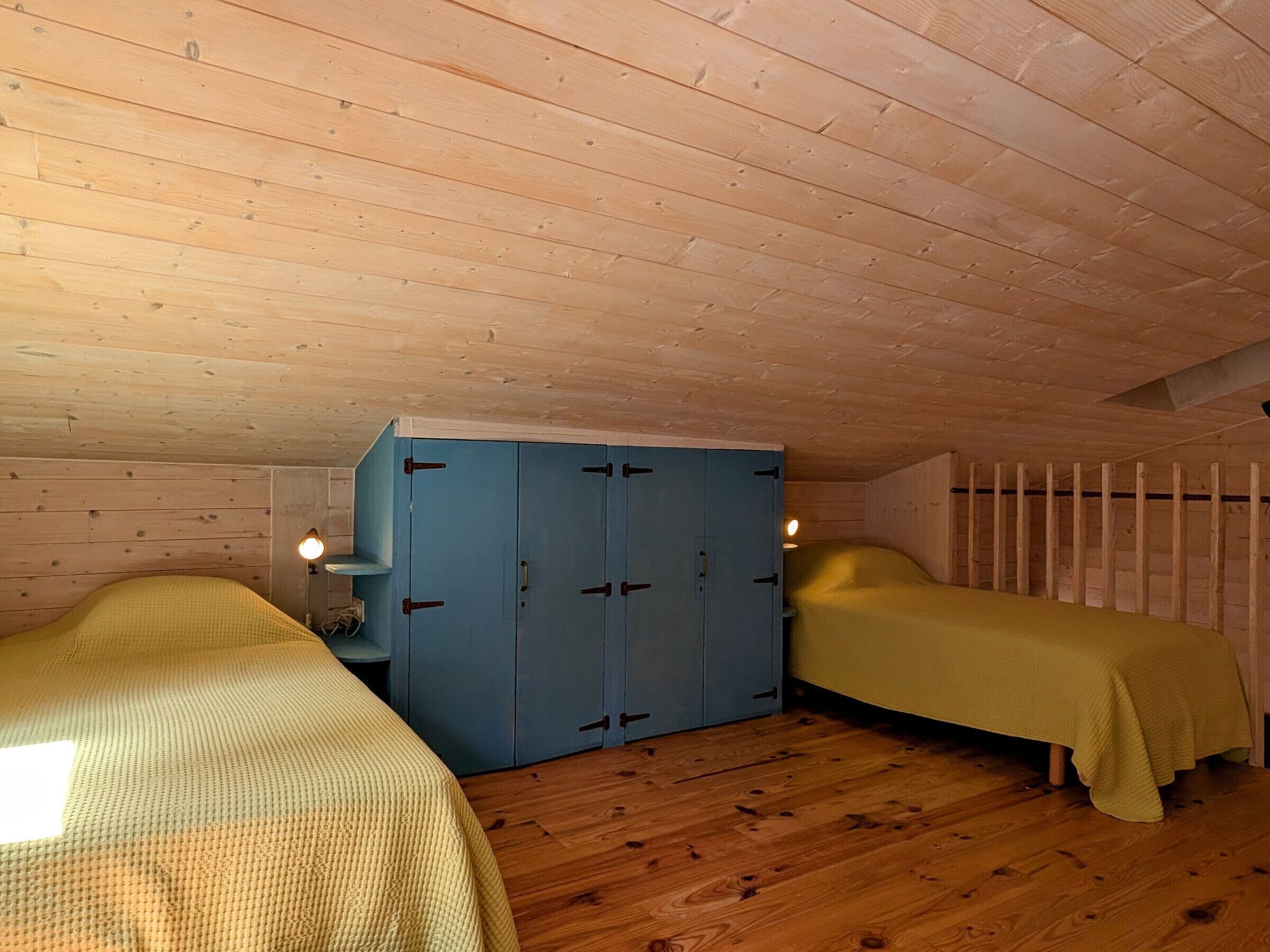 Une chambre avec deux lits, une armoire bleue, des murs en bois et un plafond en pente.