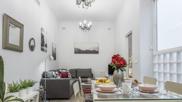 A modern living room with a glass dining table, grey sofa, and a chandelier. - Modern & quiet apartment in typical Sevilla house (Sevilla)