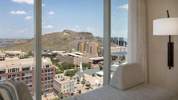 A hotel room with a large window offering a view of a cityscape, including buildings and a hill.