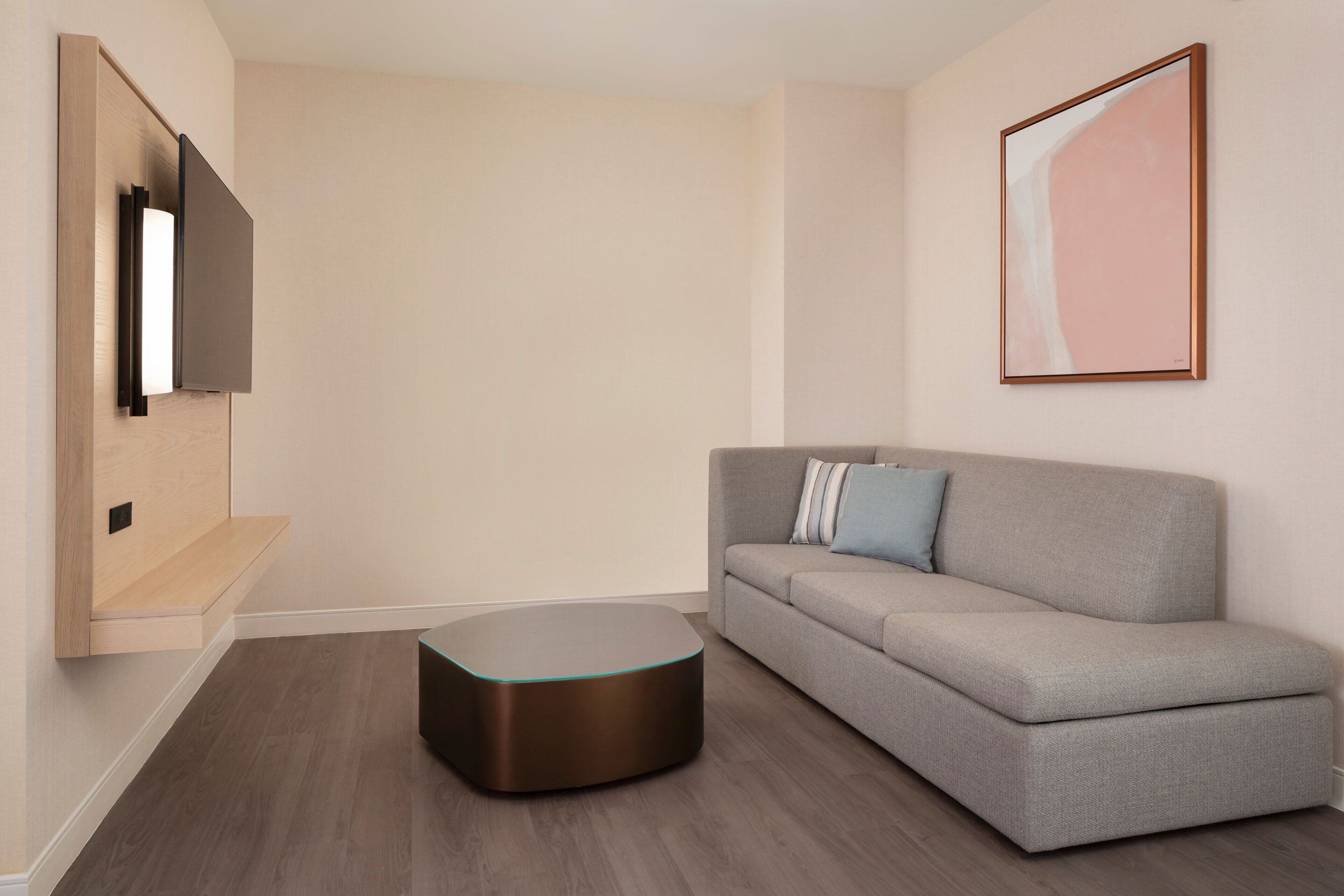 A modern living room with a grey sofa, a round coffee table, a mounted TV, and a framed abstract painting on the wall.