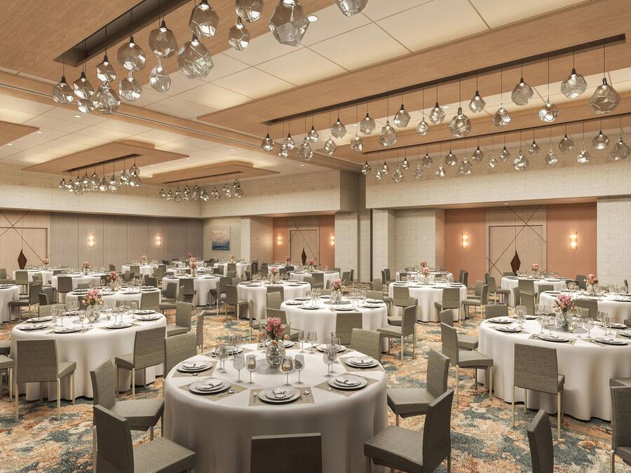 A large banquet hall with round tables set for dining, featuring a modern chandelier and neutral color scheme.