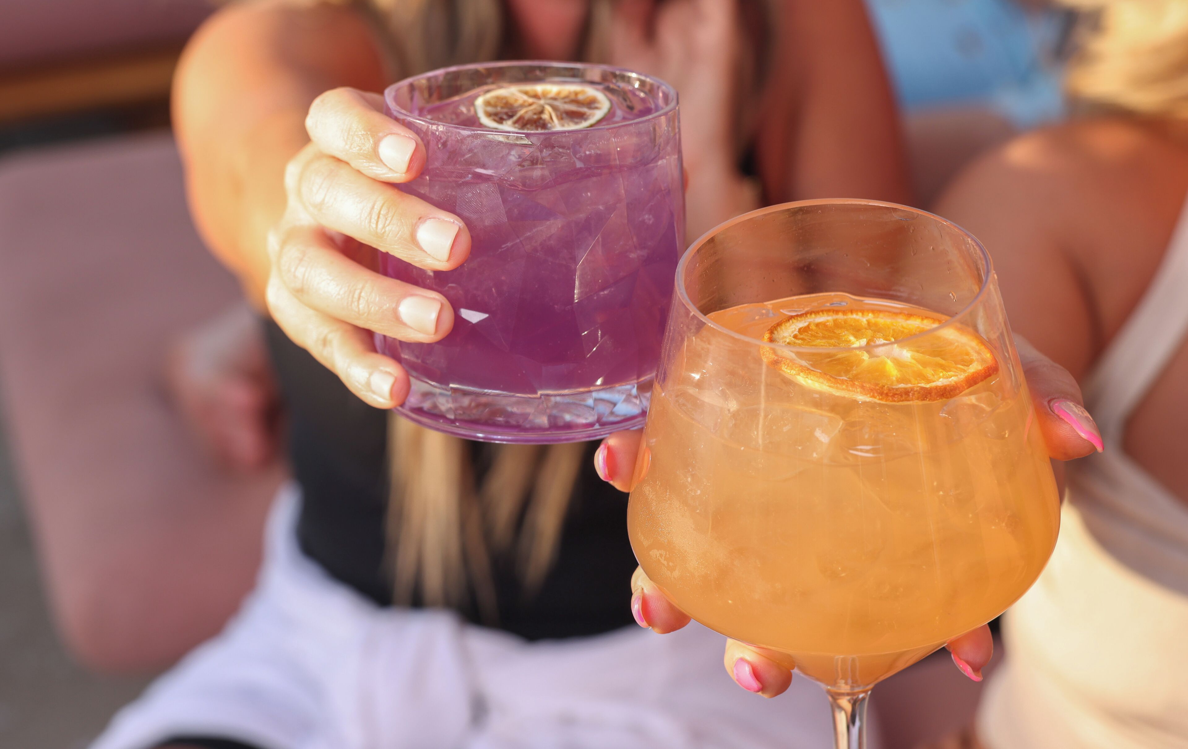 Two drinks in glasses, one purple and one orange, held by a person.