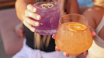 Two drinks in glasses, one purple and one orange, held by a person.