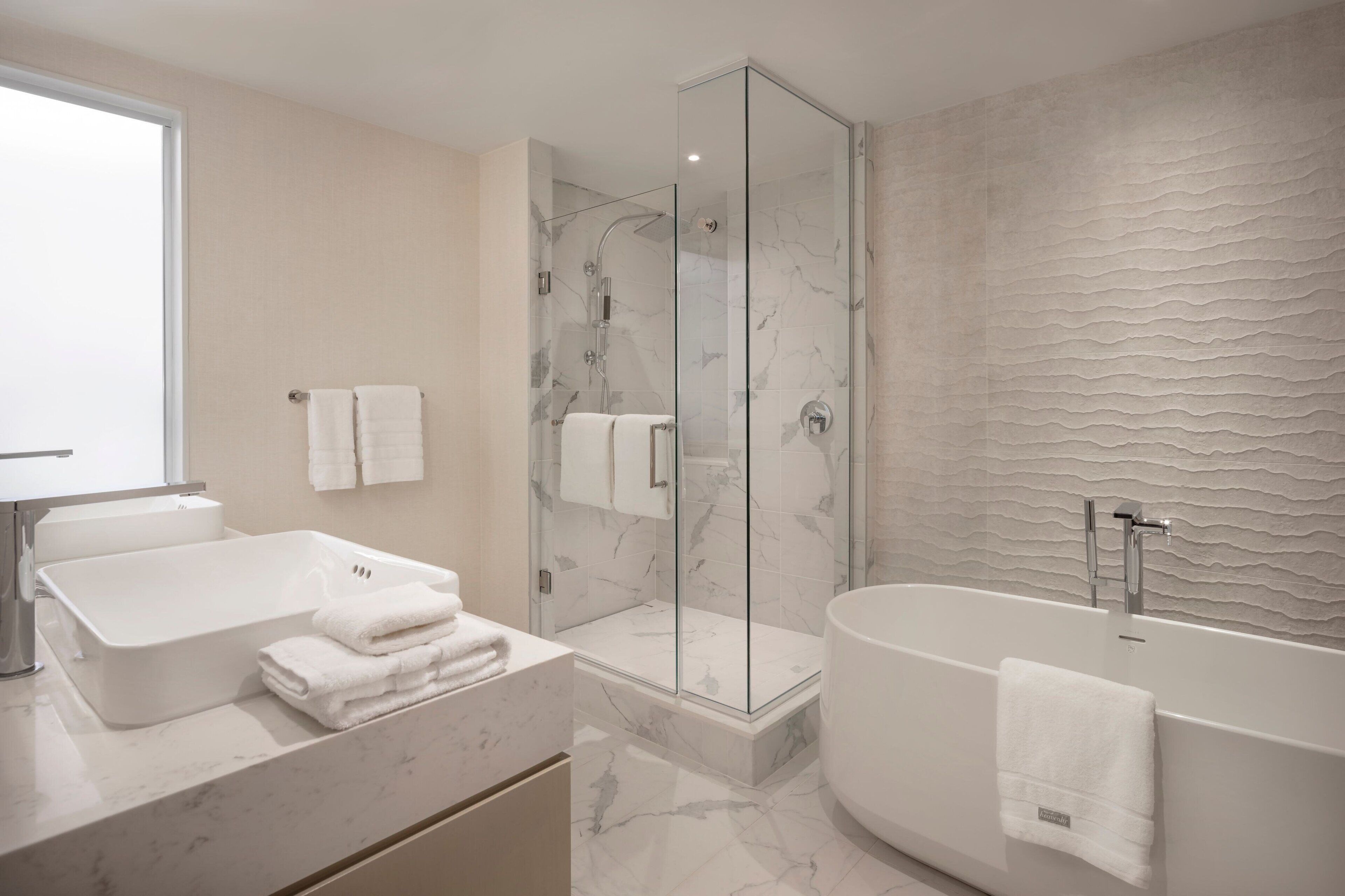 A modern bathroom with a glass-enclosed shower, a freestanding bathtub, and a marble vanity.