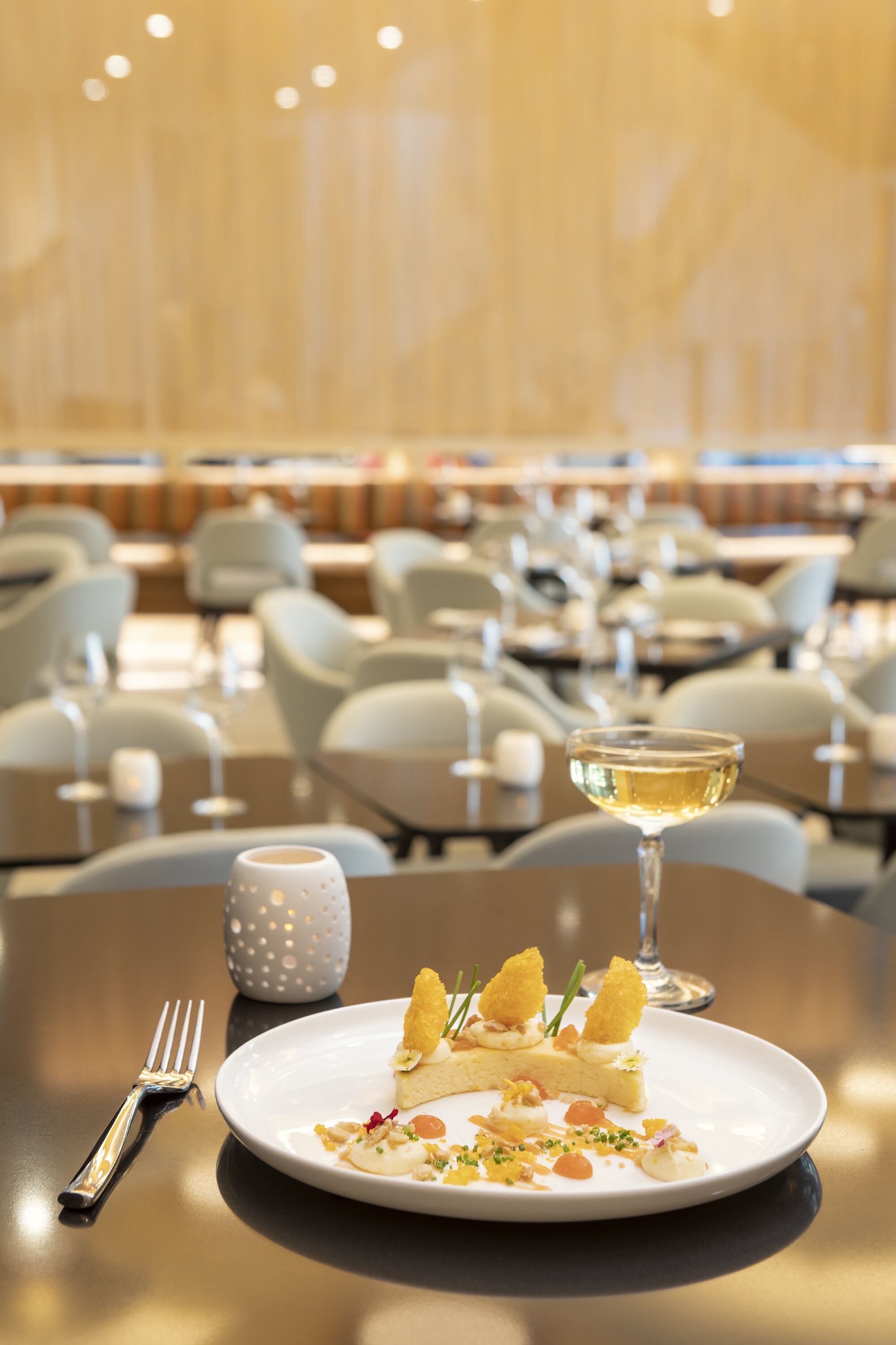 Una mesa de comedor con un plato de comida, una copa de vino blanco y un tenedor.