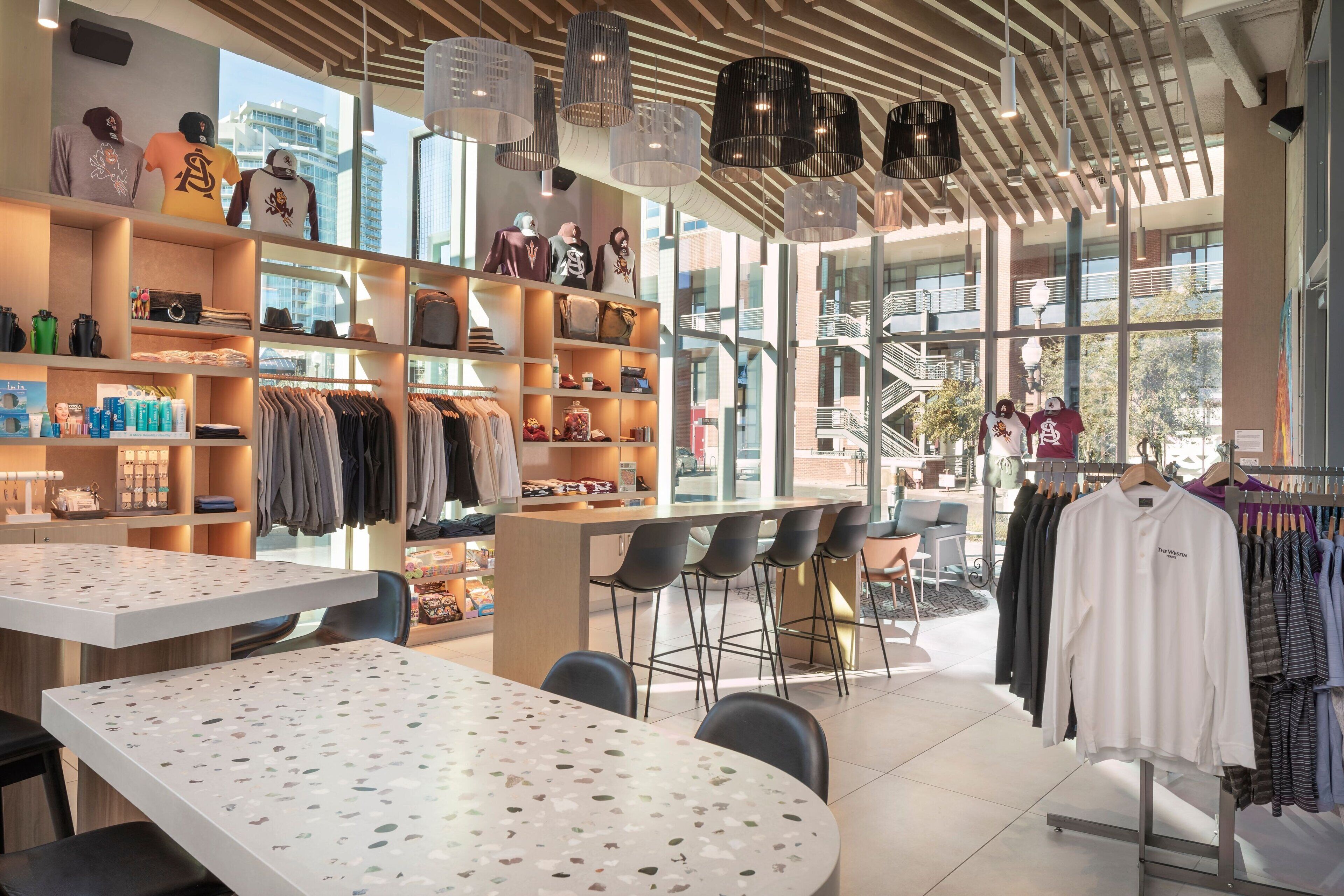 A modern retail space with clothing racks, shelves with accessories, and a bar area with stools.