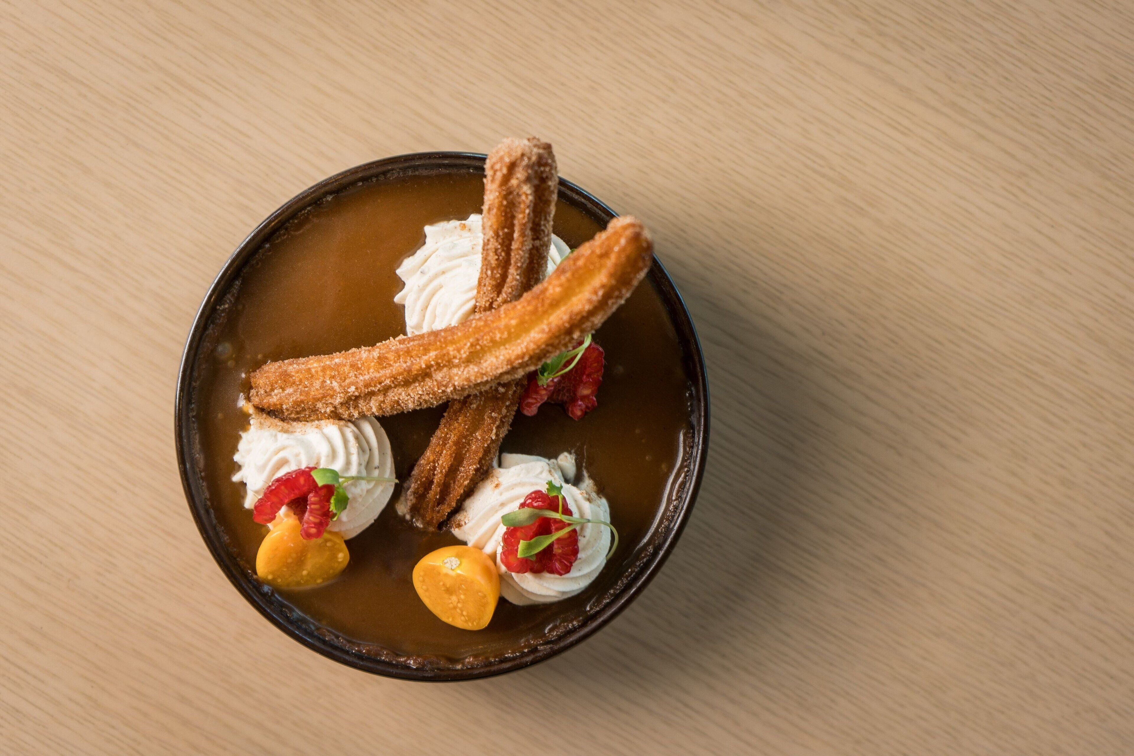 A dessert plate with churros, whipped cream, and fruit garnishes.