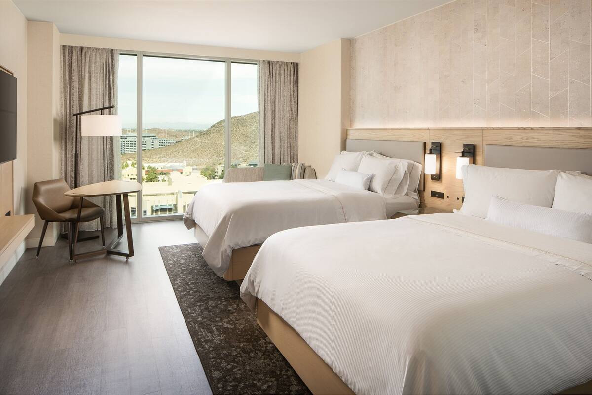 A hotel room with two beds, a desk, and a view of a mountainous landscape.