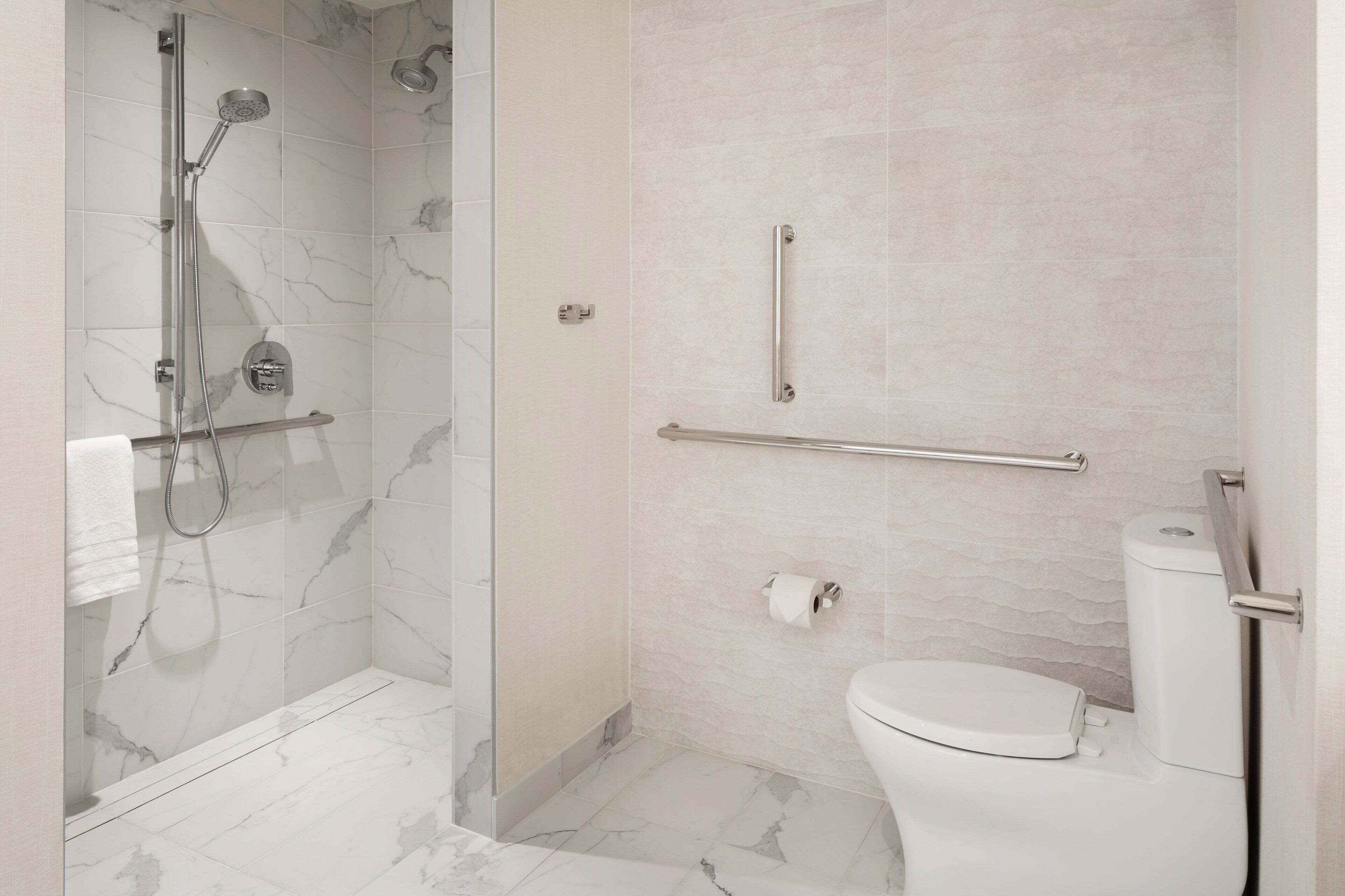 A modern bathroom with a shower, toilet, and grab bars.