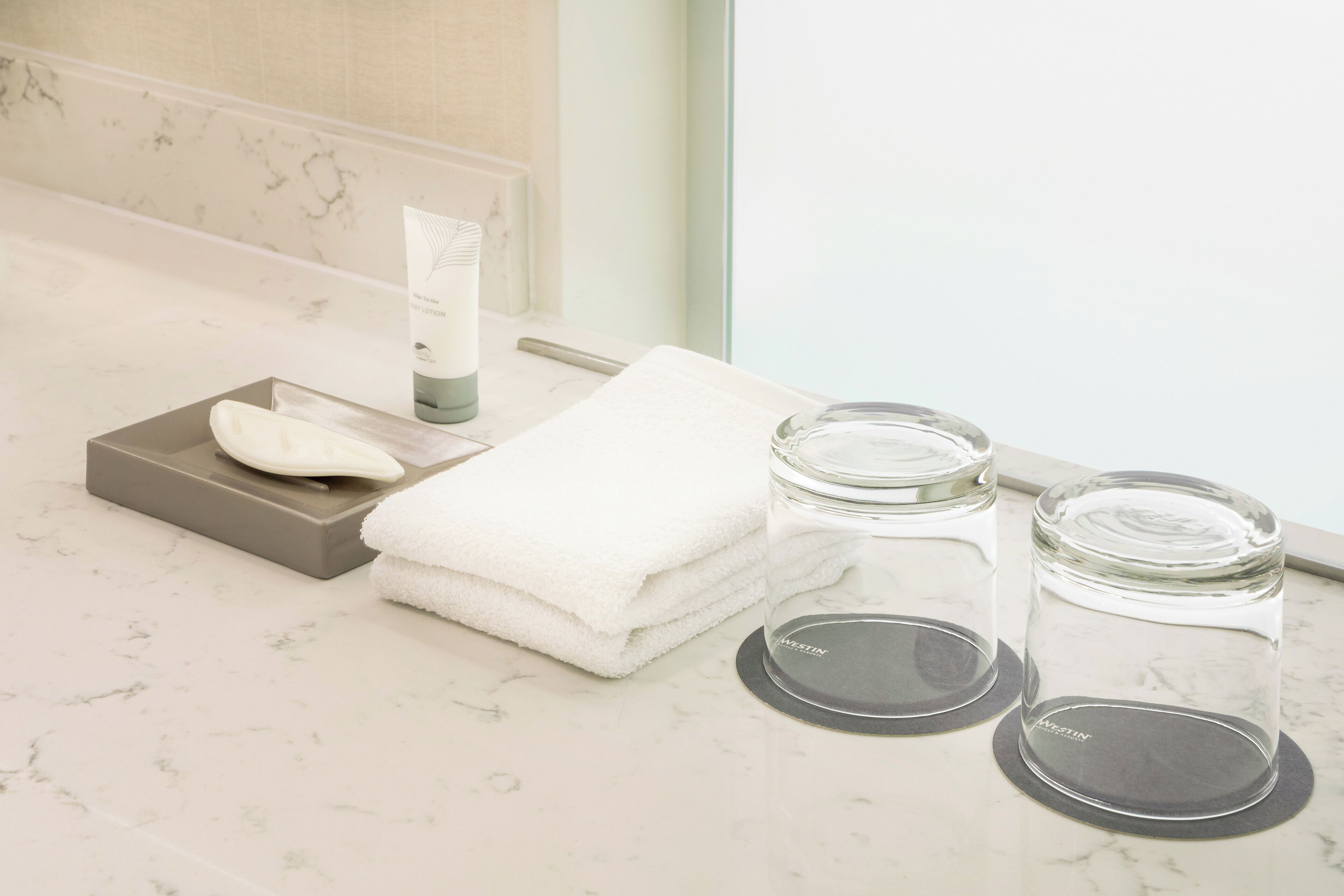 A bathroom vanity with a marble countertop, a soap dish, a towel, and two glass jars with lids.