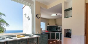 A kitchen with a view of the sea, a clock on the wall, and a window with a bowl of pastries. - Villa Esmeralda with private heated pool, sauna and great view (Salobreña)