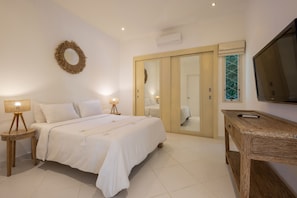 A bedroom with a bed, bedside lamps, a wooden nightstand, a mirror, a wardrobe, and a TV on the wall. - AV Villa Casabola (Seminyak)