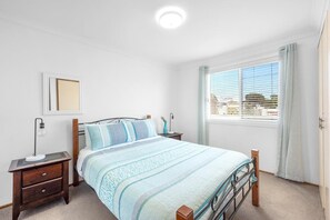 A bedroom with a bed, bedside tables, a nightstand, a window with blinds, and a ceiling light.