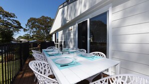 Ein Essbereich im Freien mit einem weißen Tisch und Stühlen, einem schwarzen Grill und einem großen Fenster mit Blick auf einen Garten.