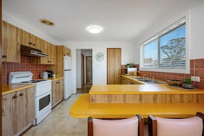 Une cuisine avec des meubles de rangement en bois, un fourneau blanc, un plan de travail jaune et une fenêtre avec des stores.