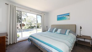 Ein Schlafzimmer mit großem Fenster, einem Bett mit gemusterten Betttextilien, einem Nachttisch und einem Gemälde an der Wand.