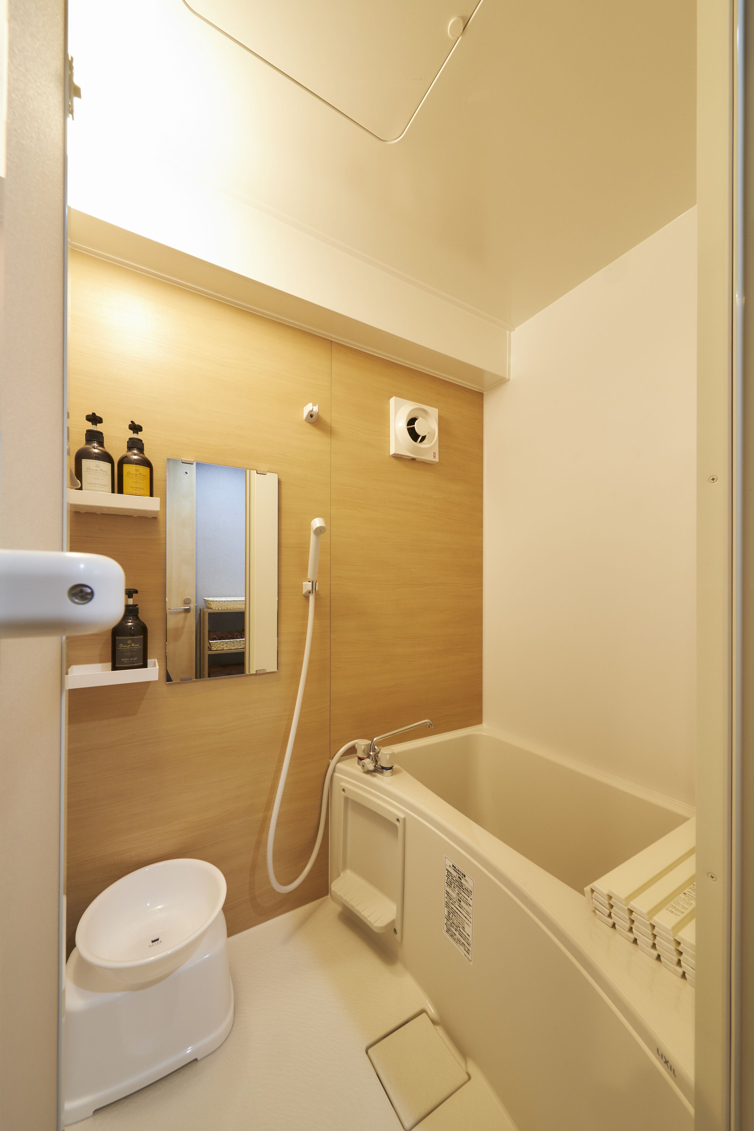 A bathroom with a toilet, sink, and bathtub. There are shelves with toiletries and a mirror above the sink.
