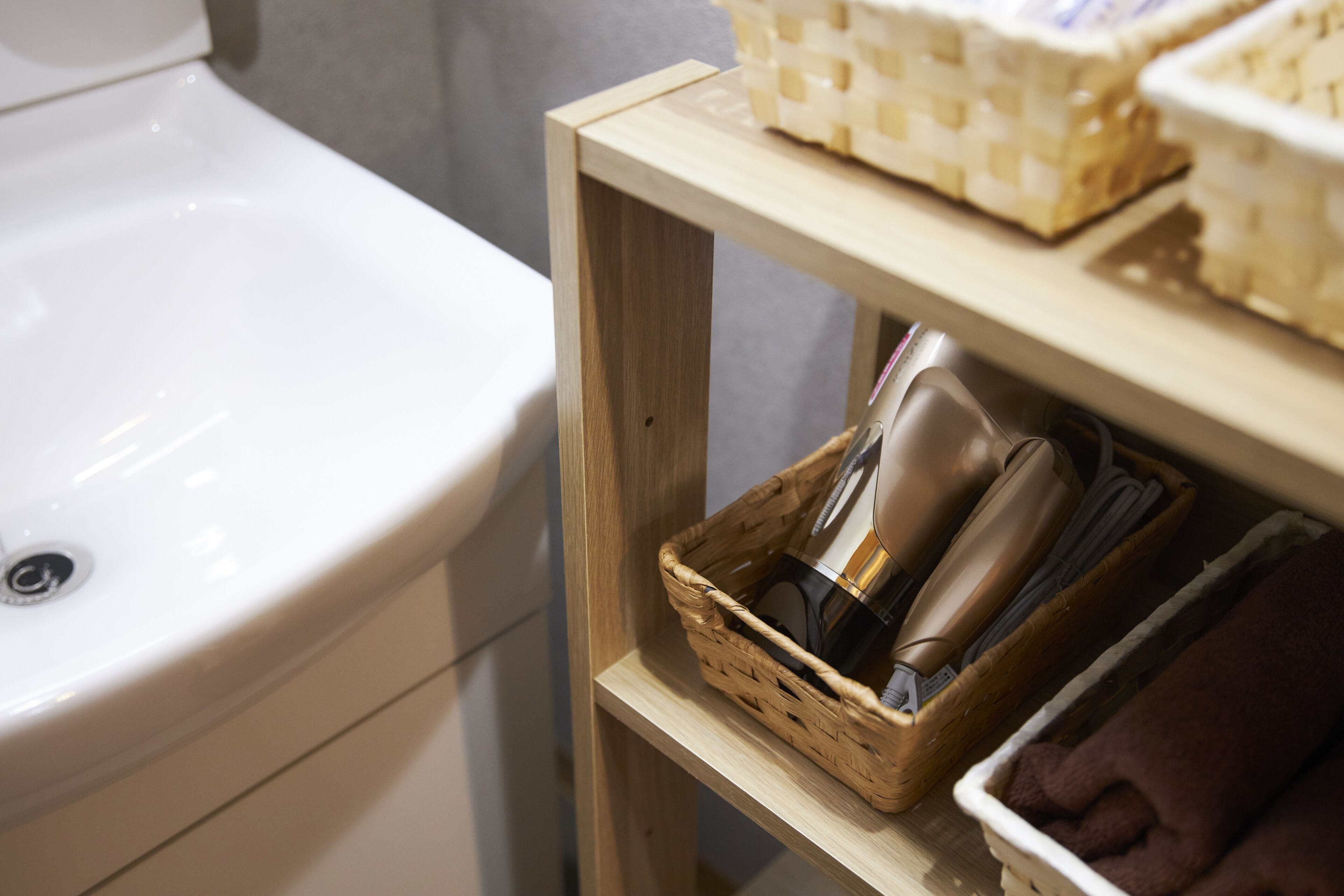 Un baño con un lavabo blanco, un estante de madera con cestas y una toalla.