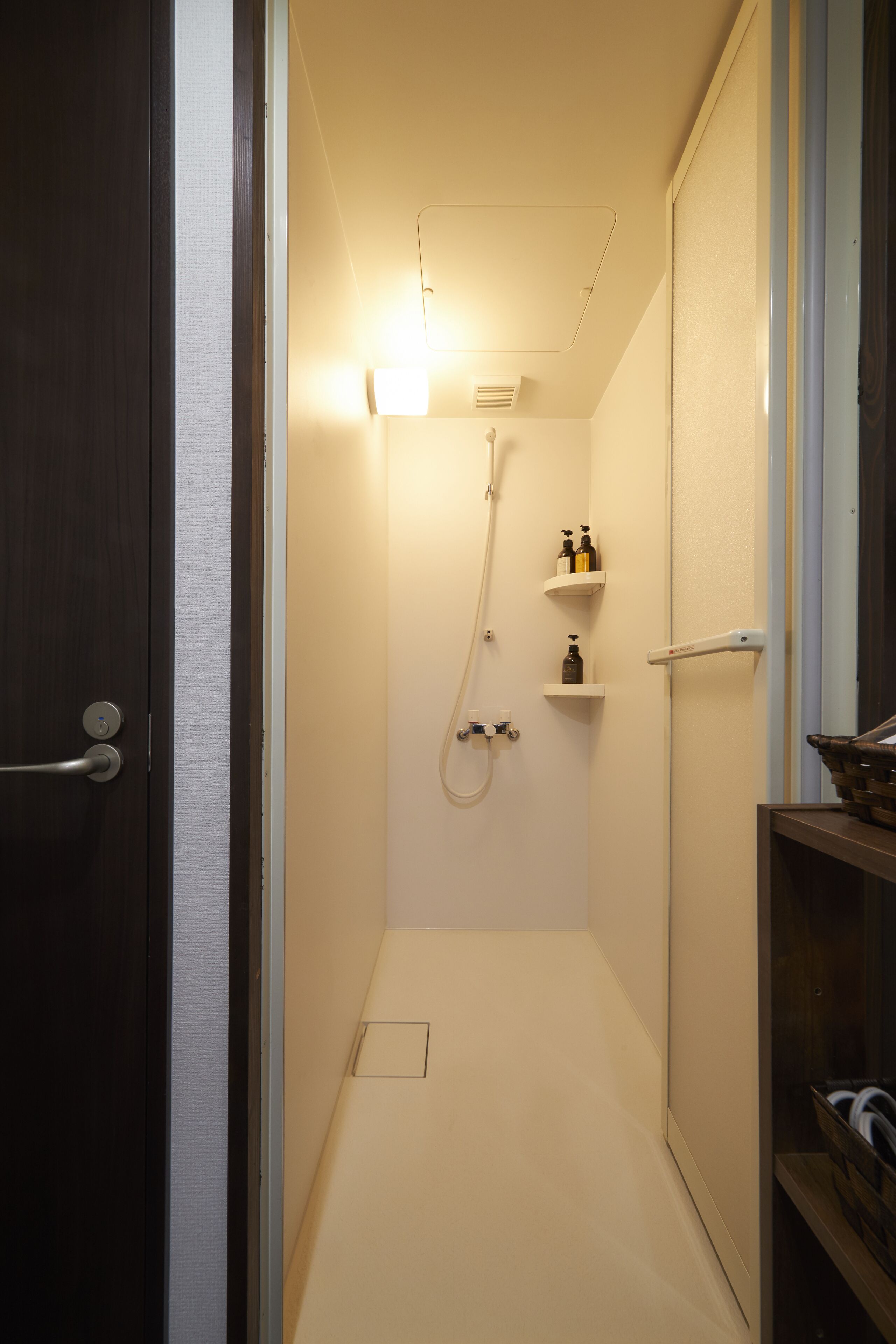 A narrow, well-lit bathroom with a shower, a towel rack, and a shelf with toiletries.