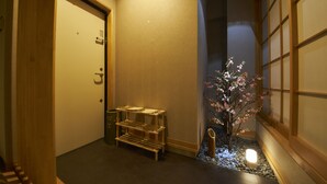 Un couloir avec une porte en bois, une petite étagère en bois et un cerisier en fleurs illuminé.