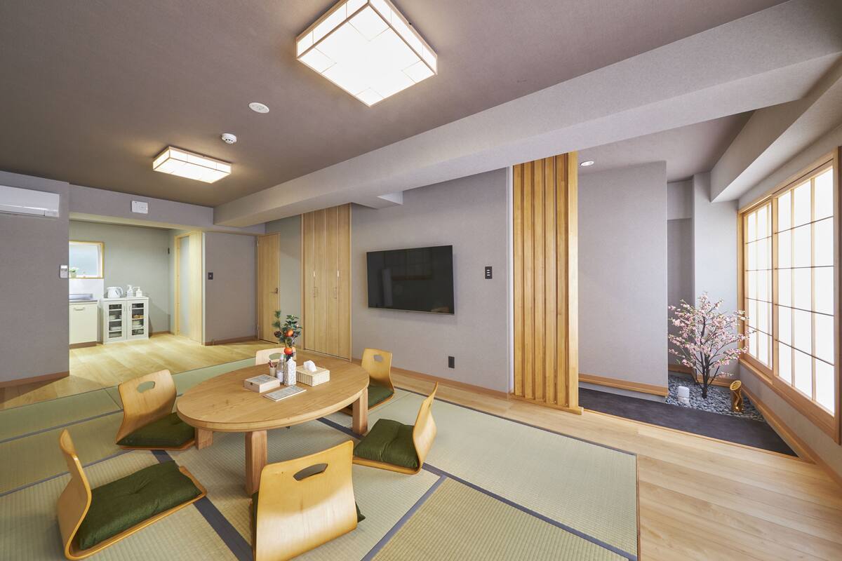 A traditional Japanese-style room with tatami flooring, a low table with cushions, and a television mounted on the wall.
