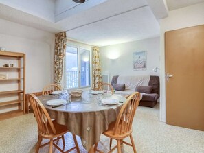 Een eethoek met een ronde tafel voor vier personen, een bank, een boekenkast en een deur.