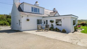 A white cottage with a small porch, two windows, and a chimney. - Charming 2 Bed House Near Rhoscolyn,discounts FOR (Holyhead)