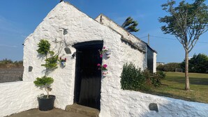 A white building with a black door, potted plants, and a tree nearby. - Charming 2 Bed House Near Rhoscolyn,discounts FOR (Holyhead)