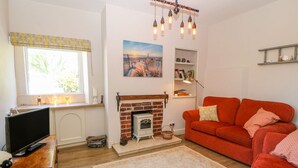 A cozy living room with a fireplace, a red sofa, a television, and a bookshelf. - Charming 2 Bed House Near Rhoscolyn,discounts FOR (Holyhead)