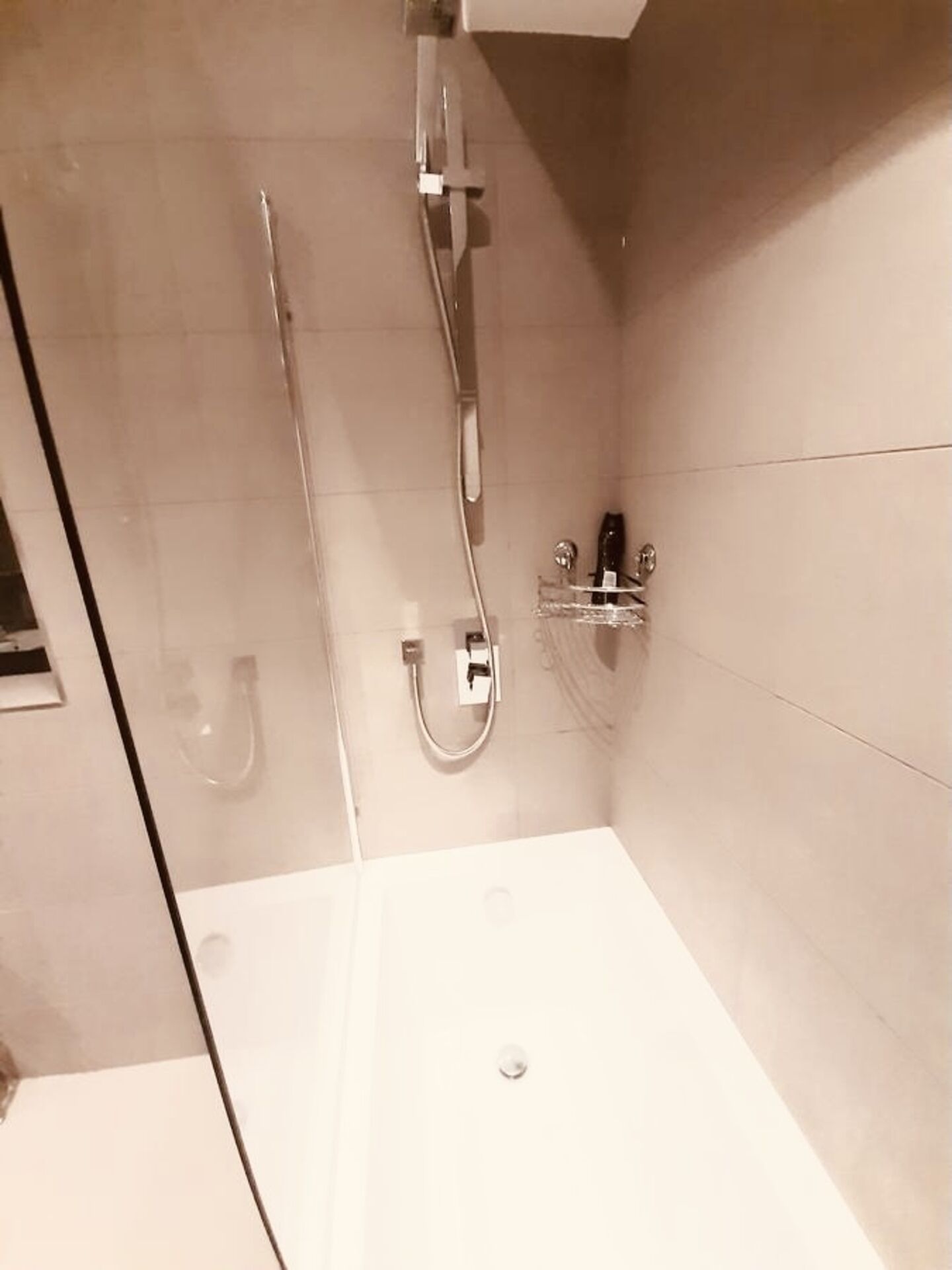 A modern bathroom with a glass-enclosed shower, a white bathtub, and a small shelf with toiletries.