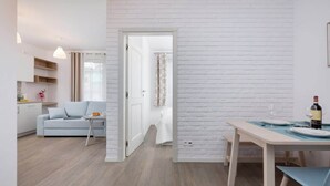 Un soggiorno moderno e open space con zona pranzo, pavimento in legno chiaro e parete decorata con mattoni bianchi.