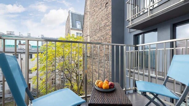 Un balcone con due sedie blu, un tavolino e una ciotola di frutta.