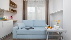Un divano moderno blu chiaro con un tablet, un piccolo tavolino con un vassoio di pasticcini e un vaso di fiori.