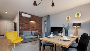 A modern living room with a dining area, featuring a brick wall, a sofa, a yellow armchair, and a dining table set for four.
